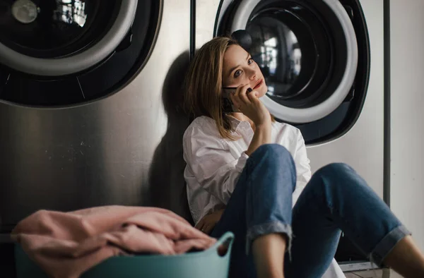 Akıllı Telefonlu Genç Bir Kadın Arıyor Çamaşırhanede Oturuyor — Stok fotoğraf
