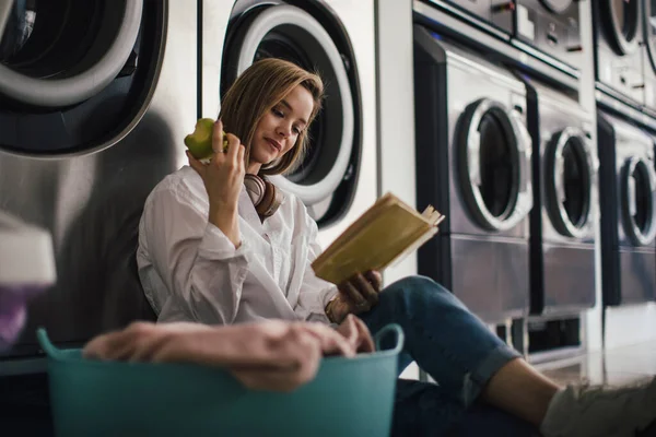 Genç Bir Kadın Kitap Okuyor Çamaşırhanede Oturuyor — Stok fotoğraf
