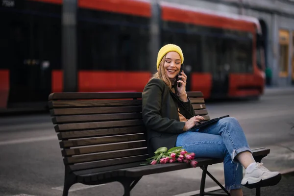 チューリップとデジタルタブレットで街に座っている若い女性 — ストック写真