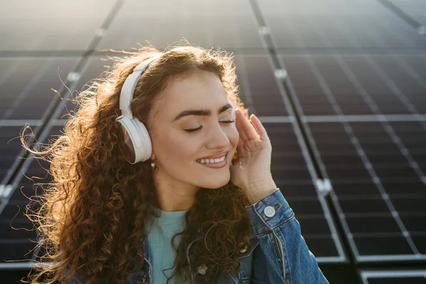 Portrait of young excited woman, owner on roof with solar panels, listening music.