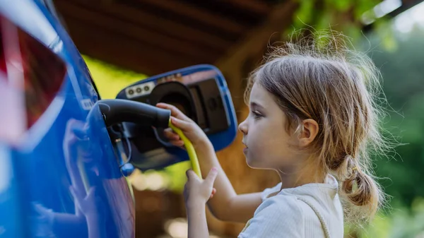 Mała Dziewczynka Trzyma Kabel Zasilający Ładuje Samochód Elektryczny — Zdjęcie stockowe