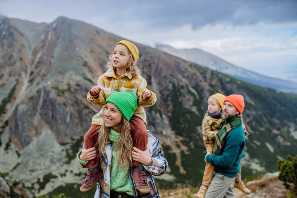 Portrait of happy family hiking together in an autumn mountains. Hiking with young kids. Mother carrying young girl on shoulders.