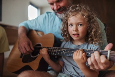 Baba ve kızı birlikte gitar çalıyorlar. Çocuklar ebeveynlerinden müzik aleti ile çalmayı öğrenirler..