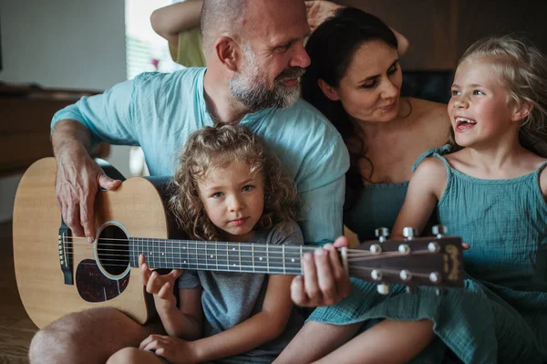 Father playing on guitar for his family. Family having fun and singing together. Concept of family bonding.