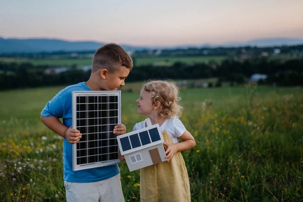 小男孩拿着太阳能电池板 他姐姐拿着装有太阳能电池板的房子模型 可再生能源 节约资源和可持续生活方式概念 站在中间的兄弟姐妹 — 图库照片