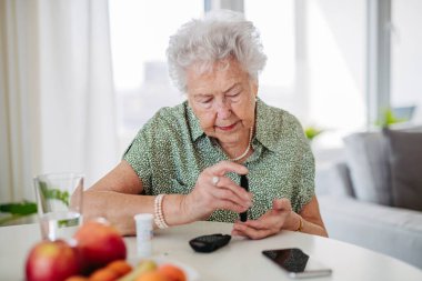Diyabetik kıdemli hasta kan şekeri seviyesini parmak ölçer ile ölçüyor. Tip 1 diyabeti olan yaşlı bir kadının portresi evde kan şekeri monitörü kullanıyor..