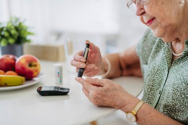 Diyabetik kıdemli hasta kan şekeri seviyesini parmak ölçer ile ölçüyor. Tip 1 diyabeti olan yaşlı bir kadının portresi evde kan şekeri monitörü kullanıyor..