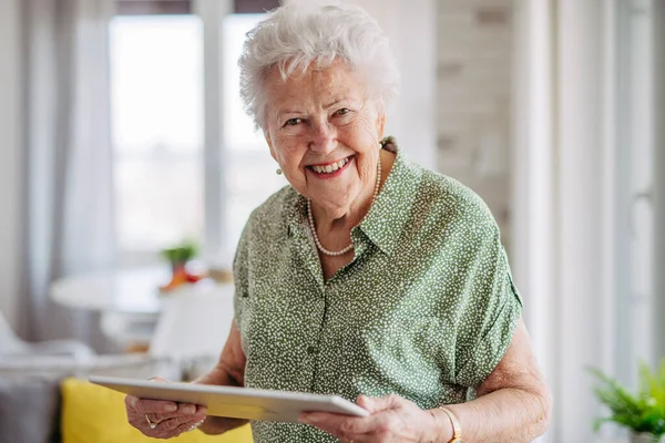 在家里手拿着石碑的漂亮老太太的画像 快乐的老妇人用平板电脑购物 打电话 看报纸或玩纸牌游戏 — 图库照片