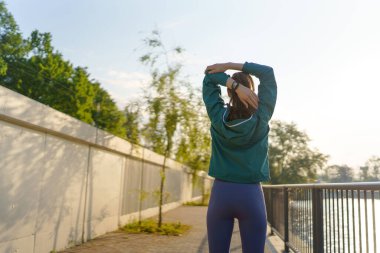 Sabah koşusundan önce gerinen genç bayan koşucunun arka görüntüsü. Spor giyim bölümündeki fitness kızı akşam egzersizi için hazırlanıyor. Açık hava idman konsepti.