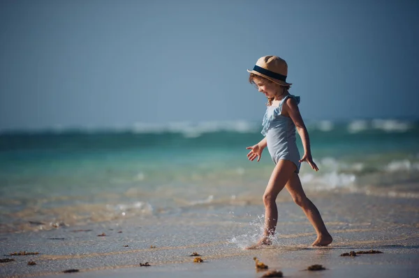 一个穿着泳衣和草帽在海滩上散步的小女孩的画像 在桑给巴尔 身穿蓝色游泳衣 满身笑容的女孩 享受着沙滩和水晶般的Mnemba海滩 — 图库照片