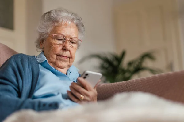 老年妇女在智能手机上浏览的肖像 家中使用流动电话的老年妇女 — 图库照片