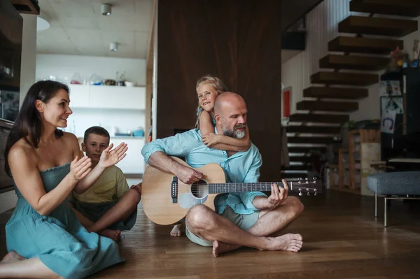Father playing on guitar for his family. Family having fun and singing together. Concept of family bonding.