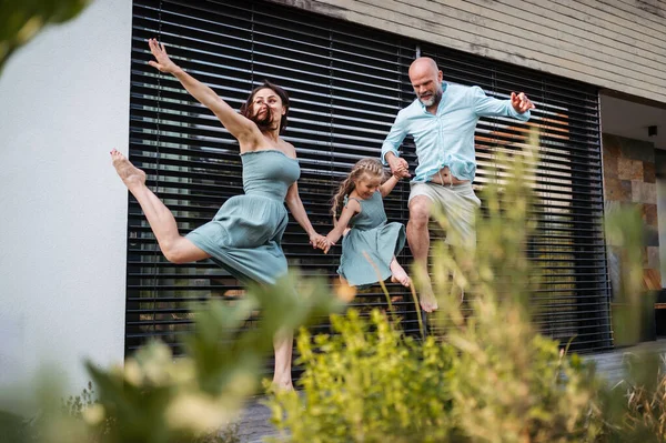 Portrait of a happy family having fun and spending time together outdoors. Mother, father and daughter holding holding hands and jumping. Concept of family bonding.
