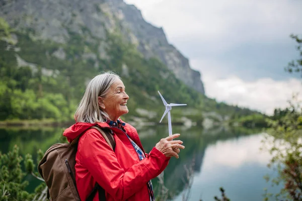 風力タービンのモデルを持っているアクティブな女性の上級観光客の肖像画 バックパックを持つシニア女性は タービンの刃を紡いでいます 再生可能エネルギーと持続可能なライフスタイルのコンセプト — ストック写真