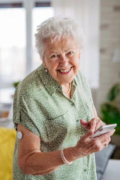老年糖尿病妇女在智能手机上查看血糖数据 笑着拿着手机的老太太 糖尿病老年患者使用连续血糖监测器检查家里的血糖水平 — 图库照片