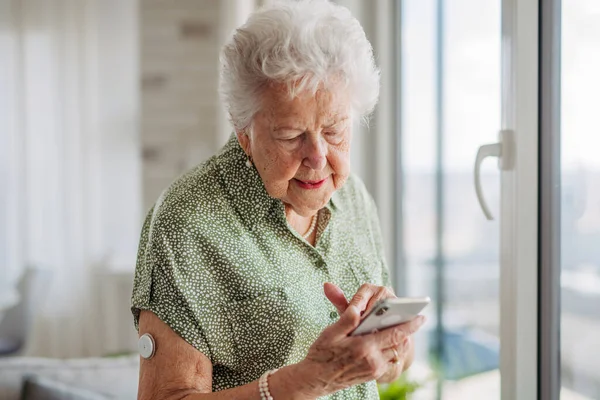 老年糖尿病妇女在手机上查看血糖数据 笑着在智能手机上打滚的老太太 糖尿病老年患者使用连续血糖监测器检查血糖水平 — 图库照片