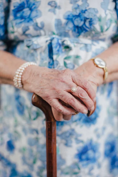 Close-up of a senior womans hands holding a walking cane. Old lady with wrinkled skin on arms and vintage jewelry.