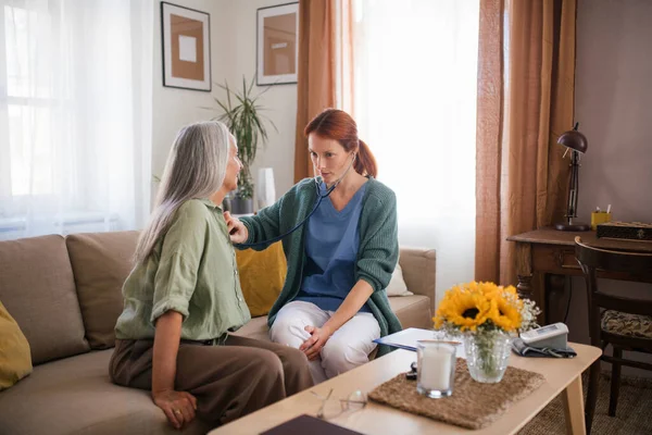 自宅でステスコープでシニア患者を診察する看護師 高齢者の呼吸と心臓を聴いている女性医師 心臓手術後のチェックイン — ストック写真