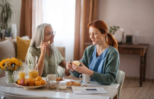 看護師は自宅で上級女性と質の高い時間を過ごし 一緒に健康的な朝食をとっています 高齢者の世話をする女性介護者 — ストック写真