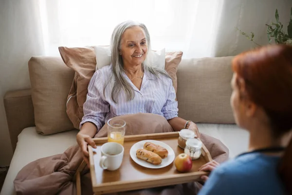 看護師はベッドで食事をし 自宅で嘘つきの患者に食事を提供している 手術後にベッドで朝食を食べるシニア女性 高齢者の世話をする女性介護者 — ストック写真
