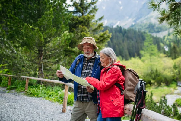 Active elderly couple hiking together in autumn mountains, on senior friendly trail. Senior spouses on the vacation in the mountains celebrating anniversary. Senior tourists with backpacks reading map