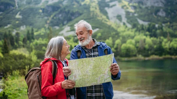 Active elderly couple hiking together in autumn mountains, on senior friendly trail. Senior spouses on the vacation in the mountains celebrating anniversary. Senior tourists with backpacks reading map