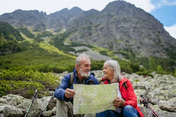 Active elderly couple hiking together in autumn mountains, on senior friendly trail. Senior spouses on the vacation in the mountains celebrating anniversary. Senior tourists sitting on rocks and