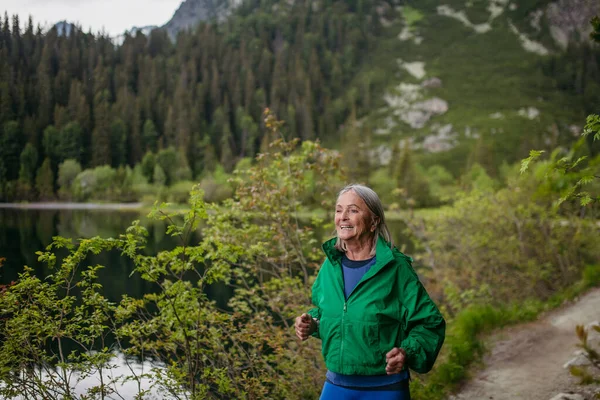 Senior runner running by the lake in the autumn. Elderly woman spending active vacation in the mountains, enjoying combination of physical activity and relaxation.