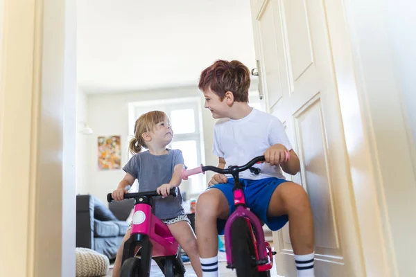 姉妹たちは家の廊下で自転車に乗っている 若い男の子と女の子は自宅で休暇中に楽しんでおり お互いに自転車でレースをしています 兄弟愛と遊びの概念 — ストック写真