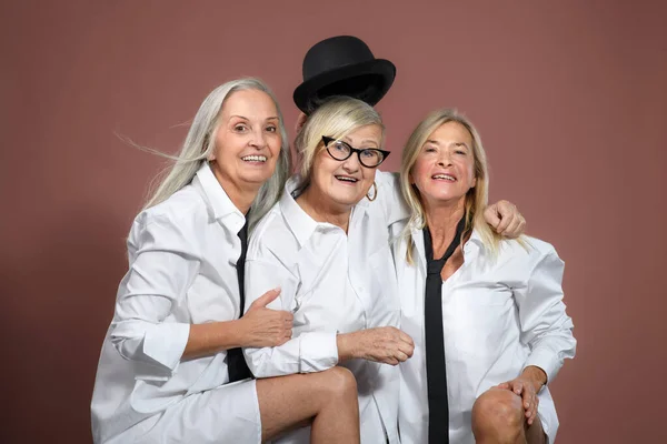 工作室的肖像三个美丽的老年妇女与白发白衬衫 年迈有趣的朋友相互牵着手 看着镜头 在棕色粉红的背景上分离 复制空间 — 图库照片