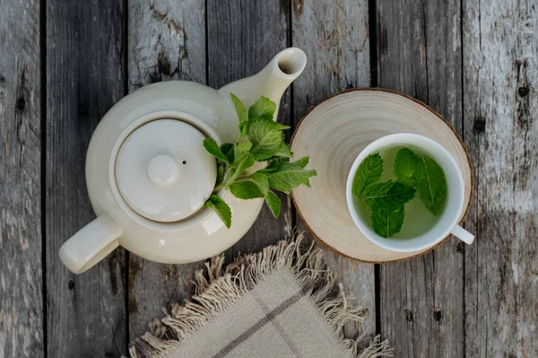 Top view of a teapot and tea cup with homemade lemon balm tea on a wooden table. Homegrown herbs are used to prepare herbal tea. Lemon balm as a medicinal herb.