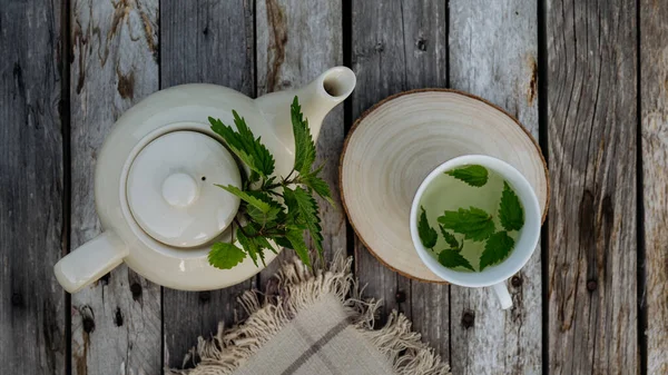 Top view of a teapot and tea cup with homemade nettle tea on a wooden table. Homegrown herbs are used to prepare herbal tea. Lemon balm as a medicinal herb.