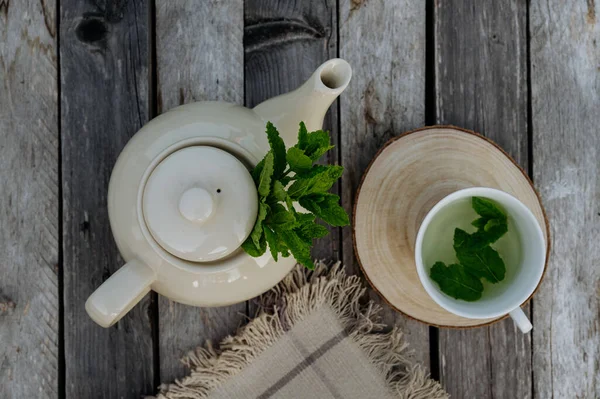 Top view of a teapot and tea cup with homemade mint tea on a wooden table. Homegrown herbs are used to prepare herbal tea. Lemon balm as a medicinal herb.