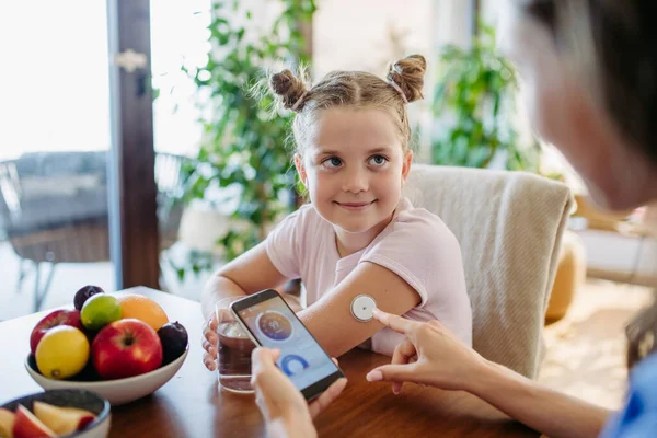 Girl with diabetes checking blood glucose level at home using continuous glucose monitor. Girls mother connects CGM to a smartphone to monitor her blood sugar levels in real time.