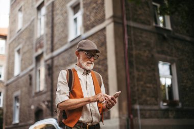 Yeni bir şehri keşfeden ve ilginç yerleri ziyaret eden kıdemli bir turist. Yaşlı bir adam elinde akıllı bir telefonla şehirde geziniyor..