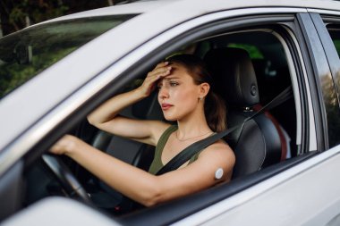 Diyabet hastası bir kadın araba sürerken başı dönüyor. CGM 'li diyabetik kadın araba kullanmaya devam etmek için kan şekerini yükseltmeli..
