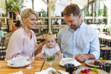 Yüksek sandalyede bebek sahibi bir aile restoranda yemek yiyor. Restoranda aile yemeği..