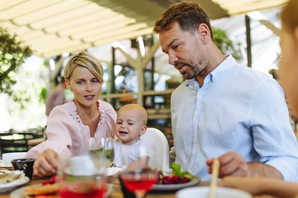 レストランで食べ物を食べる高い椅子に飢えた赤ん坊を持つ家族 レストランでのファミリーディナー — ストック写真
