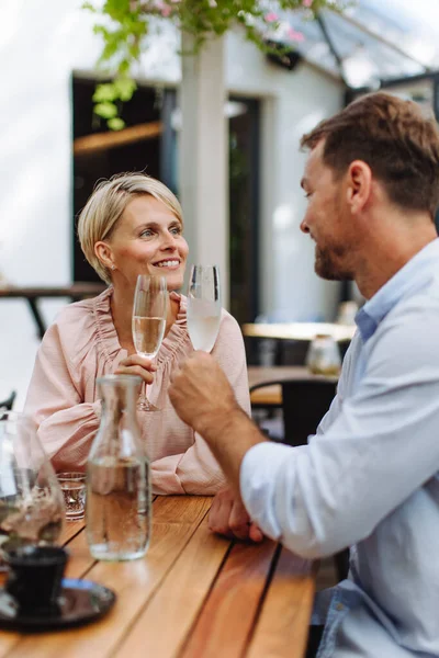 Portrait of beautiful couple in a restaurant, on a romantic date. Husband and wife are clinking champagne glasses, making a toast at restaurant patio.