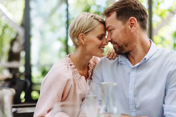 Portrait of beautiful couple in a restaurant, on a romantic date. Wife and husband touching foreheads, having a romantic moment at restaurant patio.