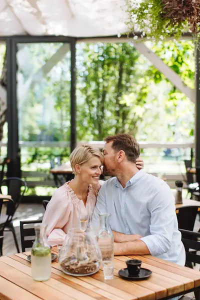 ロマンチックなデートで レストランで美しいカップルの肖像画 夫は彼の妻の耳にささやき レストランのパティオでロマンチックな瞬間を持っています — ストック写真