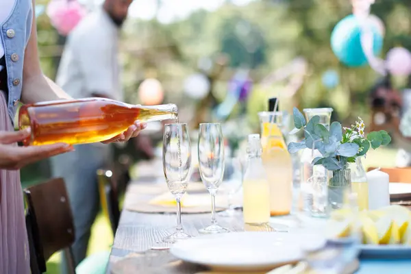 Close up shot of pouring wine at summer garden party. Table setting with glasses, lemonade and bottles of summer wine.