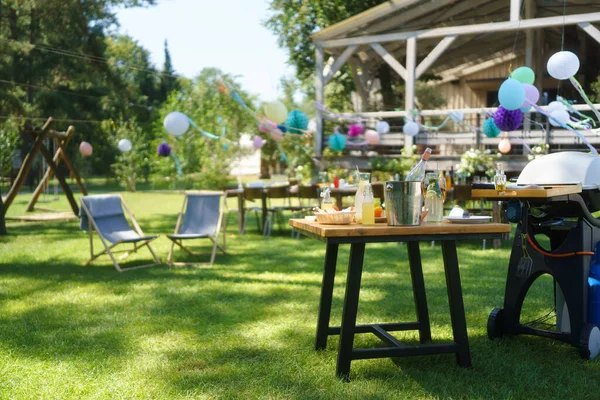 Summer garden party in a beautiful garden with a large wooden deck in the background. BBQ family gathering, with a set table and colorful decorations.