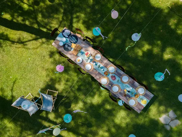 Top view of summer garden party in a beautiful garden. BBQ family gathering, with a set table and colorful decorations.