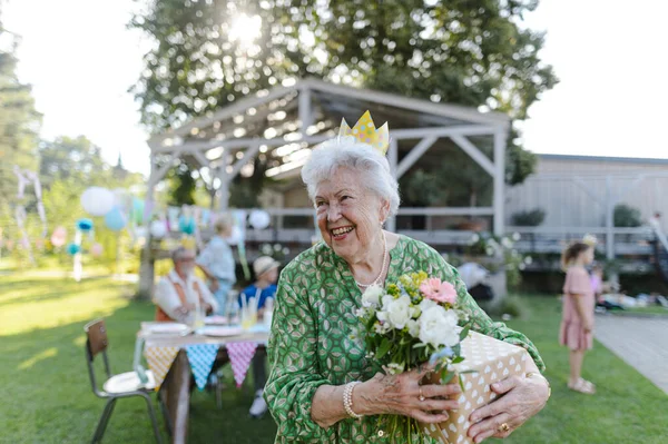 Garden birthday party for senior lady. Beautiful senior birthday woman with paper crown on head.