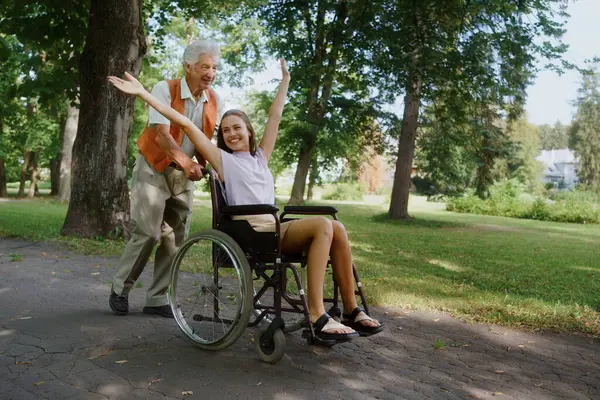 Starszy Mężczyzna Pchający Młodą Opiekunkę Wózku Inwalidzkim Bawiący Się Starszy — Zdjęcie stockowe