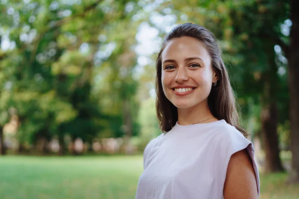 Portrait of a beautiful young woman standing outside in a city park, with copy space. The smiling woman standing with her arms crossed, looking at camera.