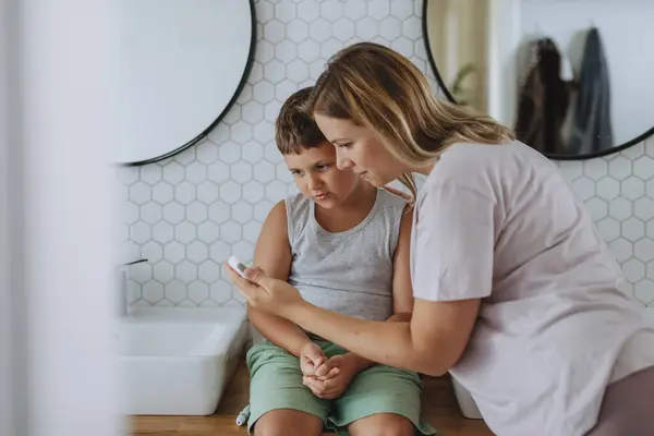 妈妈在家里用指纹计检查儿子的血糖水平 那个糖尿病男孩在等血液检测结果 妈妈爱抚她儿子的脸颊 — 图库照片