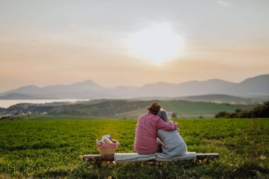 Sonbahar doğasında gün batımını izleyen yaşlı çifti kucaklıyorum. Huzurlu manzaraya bakan yaşlı eşler, High Tatras 'ın güzel manzarasının tadını çıkarıyorlar..