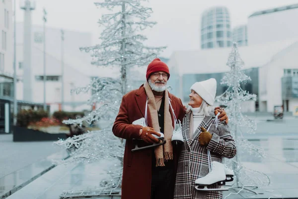 Portrait of seniors in winter at an outdoor ice skating rink. Beautiful elderly woman and man holding new ice skates.